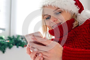 Christmas online shopping, work and education. Woman with mobile phone at home in Santa hat. Winter holidays sales.