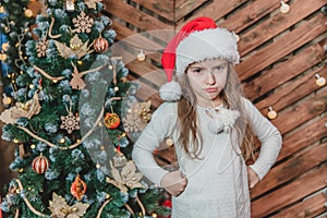 Disappointed little girl wearing Christmas costume standing isolated over wooden christmas background, keeping arms