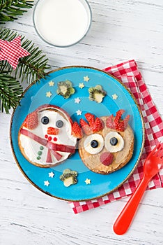 Christmas pancakes in a shape of deer and snowman made of fresh fruits and berries and glass of milk. Healthy food for kids ideas