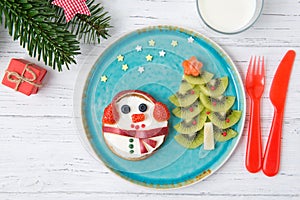 Christmas pancakes in a shape of snowman made of fresh fruits and berries and kiwi christmas tree. Glass of milk. Healthy food for