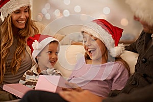 Christmas, parents and children with gift box on sofa with excited, happy celebration and surprise together. Holiday