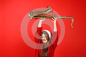 Christmas party, cheerful young woman musician fooling around with saxophone on red background