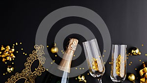 Christmas party concept. Flat lay composition with champagne bottle, glasses, golden decorations, balls, carnival mask on black