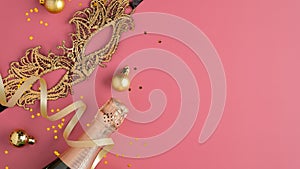 Christmas party concept. Golden ball decorations, carnival mask, champagne bottle, confetti on pink background. Flat lay, top view