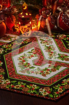 Christmas patchwork napkin, christmas candle holder with flaming candle inside and christmas decorations blurred on back view