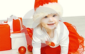 Christmas and people concept - cute smiling child in santa red hat with boxes gifts