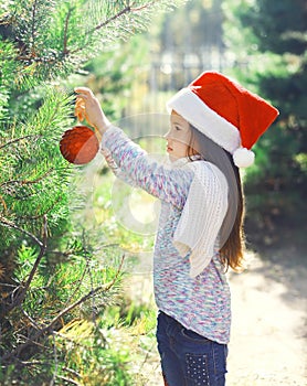 Christmas and people concept - little girl child in santa hat with ball