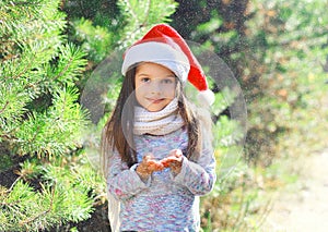 Christmas and people concept - little girl child in santa red hat blowing snow in hands