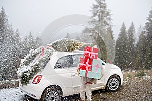 Christmas photo card of a woman with presents and car in mountains on snowy weather