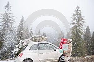 Christmas photo card of a woman with presents and car in mountains on snowy weather