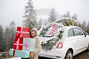 Christmas photo card of a woman with presents and car in mountains on snowy weather