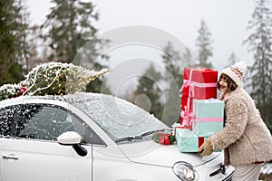 Christmas photo card of a woman with presents and car in mountains on snowy weather