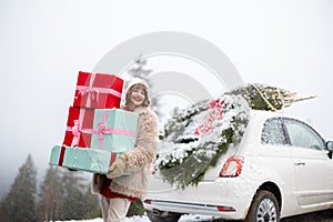 Christmas photo card of a woman with presents and car in mountains on snowy weather