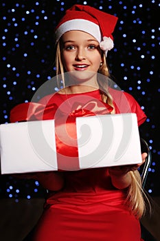 Christmas photo of cute little blond girl in santa hat and red dress holding a gift - box on the backgroud of holiday shining ligh