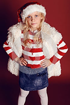 Christmas photo of cute little girl with long blond hair in Santa hat,fur coat smiling and posing in the studio