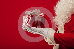 Christmas Photo of Santa Claus gloved hand with giftbox, on a red backgro