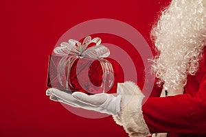 Christmas Photo of Santa Claus gloved hand with giftbox, on a red backgro