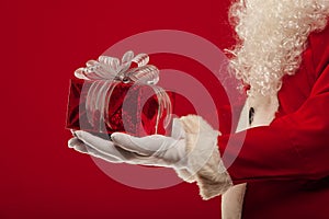 Christmas Photo of Santa Claus gloved hand with giftbox, on a red backgro