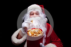 Christmas. Photo of Santa Claus gloved hand With a red bucket with popcorn, on a black background