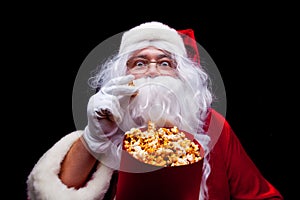 Christmas. Photo of Santa Claus gloved hand With a red bucket with popcorn, on a black background