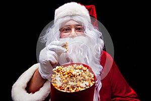 Christmas. Photo of Santa Claus gloved hand With a red bucket with popcorn, on a black background