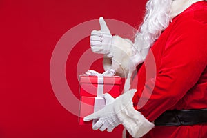 Christmas Photo of Santa Claus gloved hand with red giftbox. thumb up