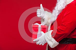Christmas Photo of Santa Claus gloved hand with red giftbox. thumb up