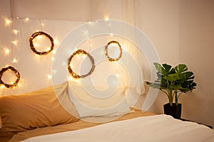 Christmas photo zone, bedroom. Bed with two pillows, home monstera plant. The walls are decorated with New Year\'s wreaths of