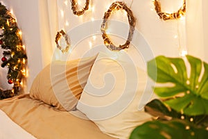 Christmas photo zone, bedroom. Bed with two pillows, home monstera plant. The walls are decorated with New Year\'s wreaths of