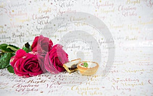 Christmas photography food image of red roses with glitter petals and mince pies on xmas wrapping paper background