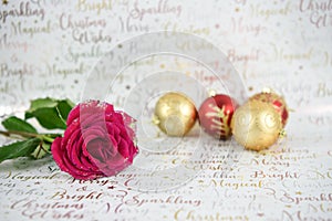 Christmas photography image of red roses with glitter petals and red gold baubles in distance on xmas wrapping paper background