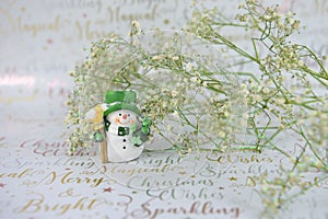 Christmas photography of white green flowers with glitter and cute happy snowman on xmas wrapping paper background