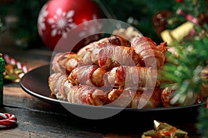 Christmas Pigs in blankets, sausages wrapped in bacon with decoration, gifts, green tree branch on wooden rustic table photo