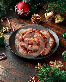 Christmas Pigs in blankets, sausages wrapped in bacon with decoration, gifts, green tree branch on wooden rustic table