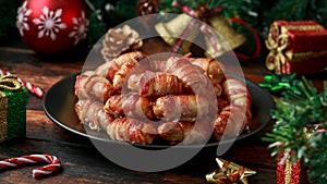 Christmas Pigs in blankets, sausages wrapped in bacon with decoration, gifts, green tree branch on wooden rustic table