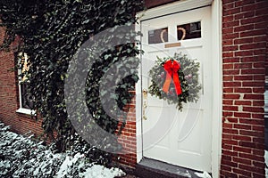 Christmas pine wreath with red bow decoration on private house door at winter time.