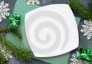 Christmas place setting with empty white plate on table with festive decorations