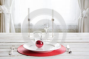 Christmas place setting with white dishware, cutlery, silverware and red decorations on white.