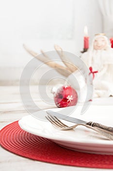 Christmas place setting with white dishware, cutlery, silverware and red decorations on wooden board. Christmas
