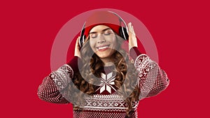 Christmas playlist. Pretty woman in warm winter clothes and headphones listening to music over red background