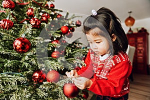 Christmas portrait of adorable 3 year old asian toddler girl wearing red Santa dress and hat