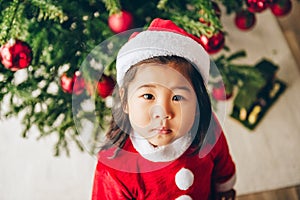 Christmas portrait of adorable 3 year old asian toddler girl wearing red Santa dress and hat