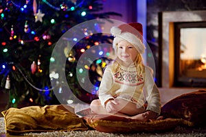 Christmas portrait of happy little girl by a fireplace in a cozy dark living room
