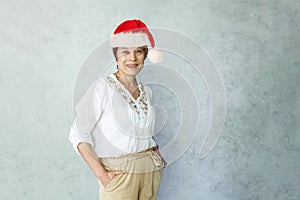 Christmas portrait of happy woman wearing red Santa hat standing against gray office wall background indoor