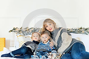 Christmas portrait of mother with her two sons laying on bed against New Year background. Cozy holiday at the fir-tree