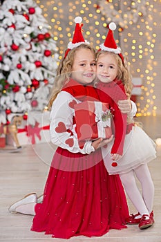 Christmas portrait of two beautyful cute girls Smiling sisters friends and xmas luxury green white tree in unique interior studio