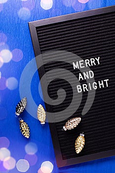 Christmas postcard. Letterboard with phrase merry and bright and golden cones decorations