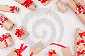 Christmas preparations - packaging gifts boxes in kraft paper with red bows and ribbons, twine on white wood table, frame.