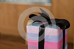 A christmas present with black bow and purple pink wrapping papper, neatly wrapped. Soft glow of christmas lights in the blurred