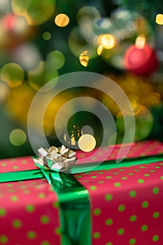 Christmas present in red paper with gold ribbon standing over christmas tree